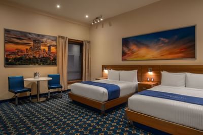 Two queen beds with a city art above the headboard and a table near a window in Double Queen Atrium at Harborside Inn Boston