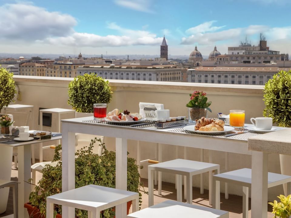 Breakfast with a View of Rome, rooftop terrace featuring white dining tables overlooking the city at The Independent