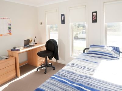Neat student bedroom with bed, desk, chair, and open windows at La Trobe University Regional Housing – Shepparton.
