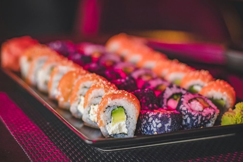 A dark plate with four long rows of sushi, the outer two with salmon, avocado, and cream cheese and the middle two with dark roe mixed into the rice.  