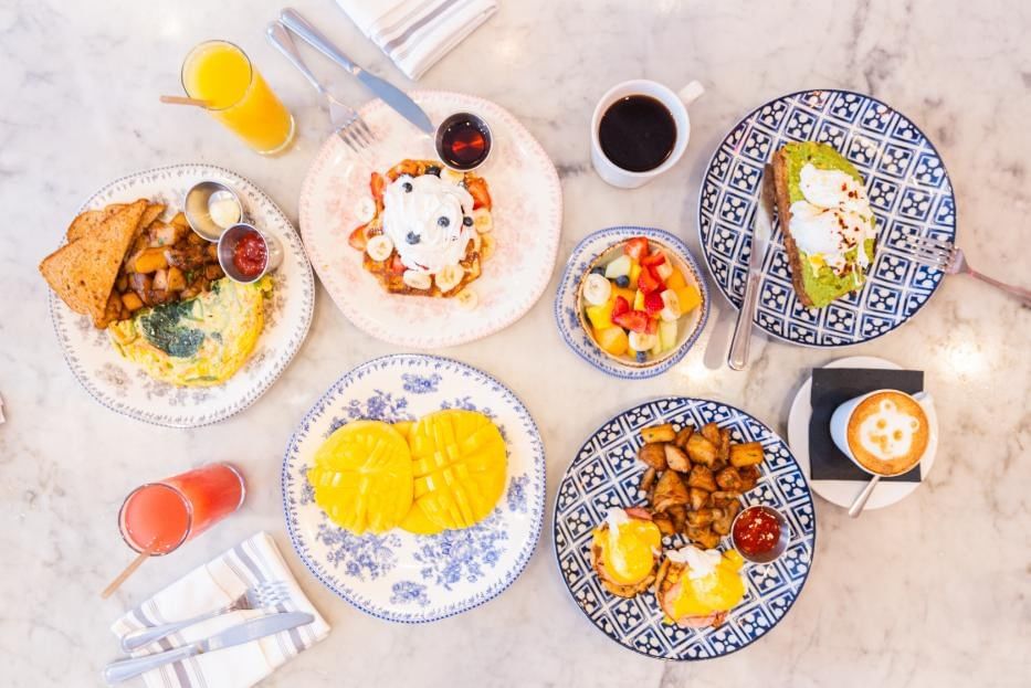A top-down view of a breakfast spread on a marble table with various plates of food and drinks.