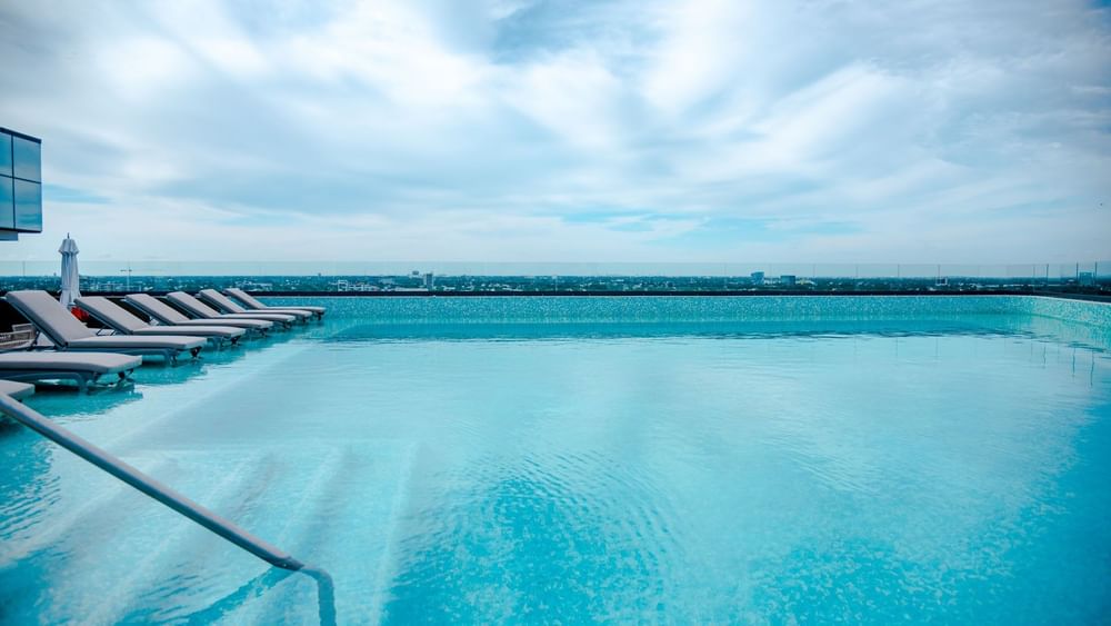 Rooftop infinity pool featuring sleek lounge chairs and a panoramic view of the city sky at Camino Real Merida