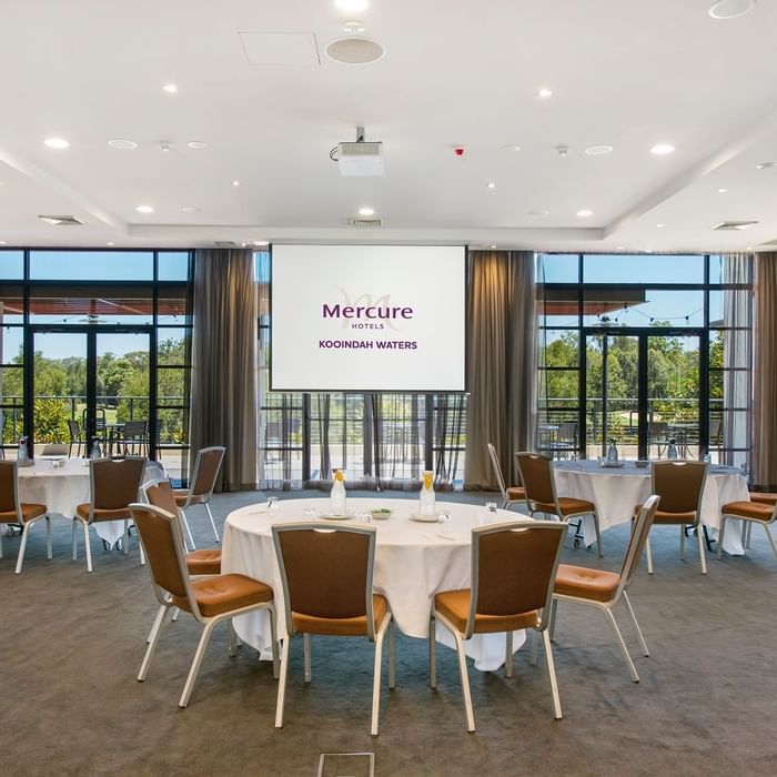 Kooindah Ballroom with tables, chairs, and large windows overlooking trees at Mercure Kooindah Waters