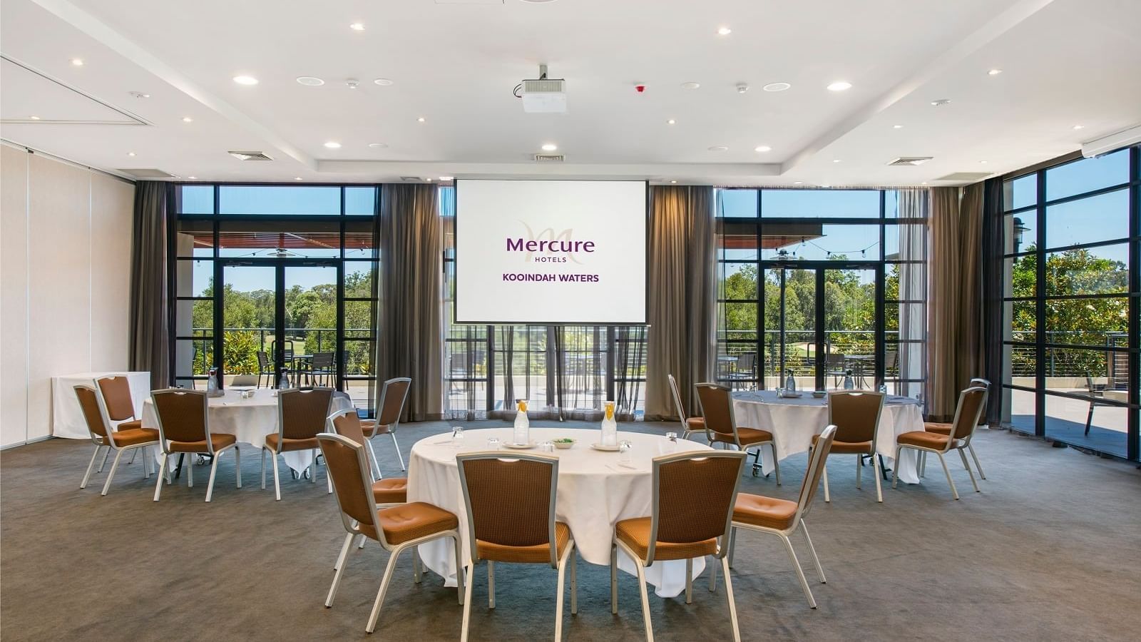 Kooindah Ballroom with tables, chairs, and large windows overlooking trees at Mercure Kooindah Waters