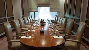 Long oval wooden table with tan chairs and white window treatments in a bright boardroom at Serena Hotels & Resorts