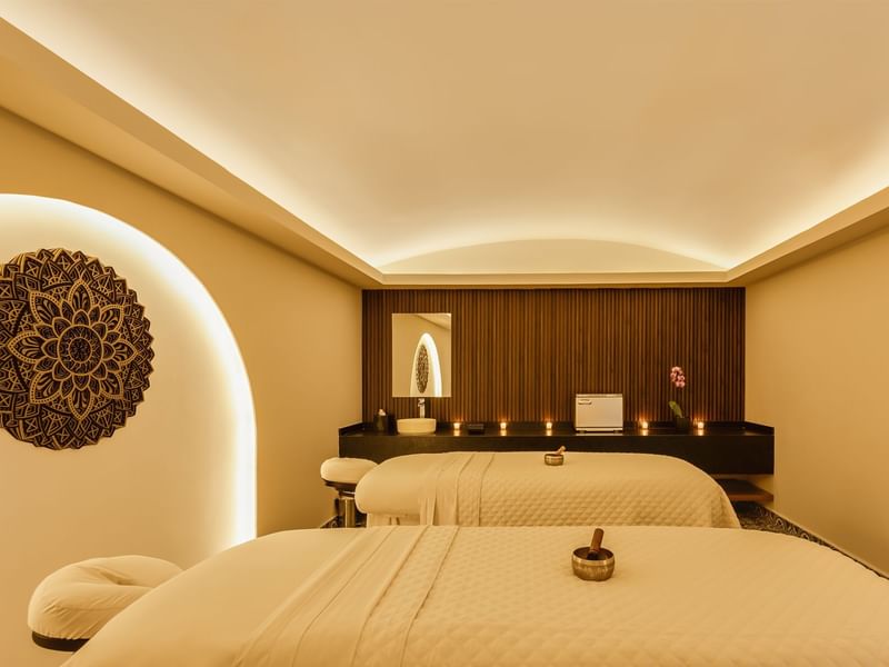 Peaceful spa treatment room at Fiesta Americana, featuring two massage beds, warm lighting, and a decorative wall mandala