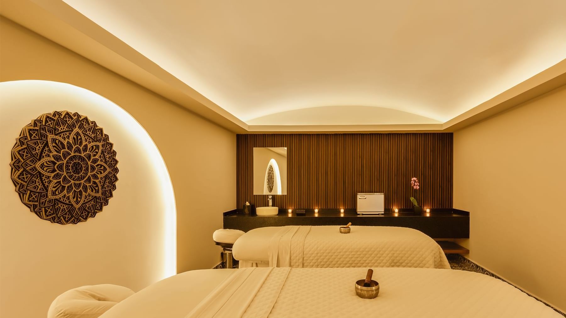 Peaceful spa treatment room at Fiesta Americana, featuring two massage beds, warm lighting, and a decorative wall mandala