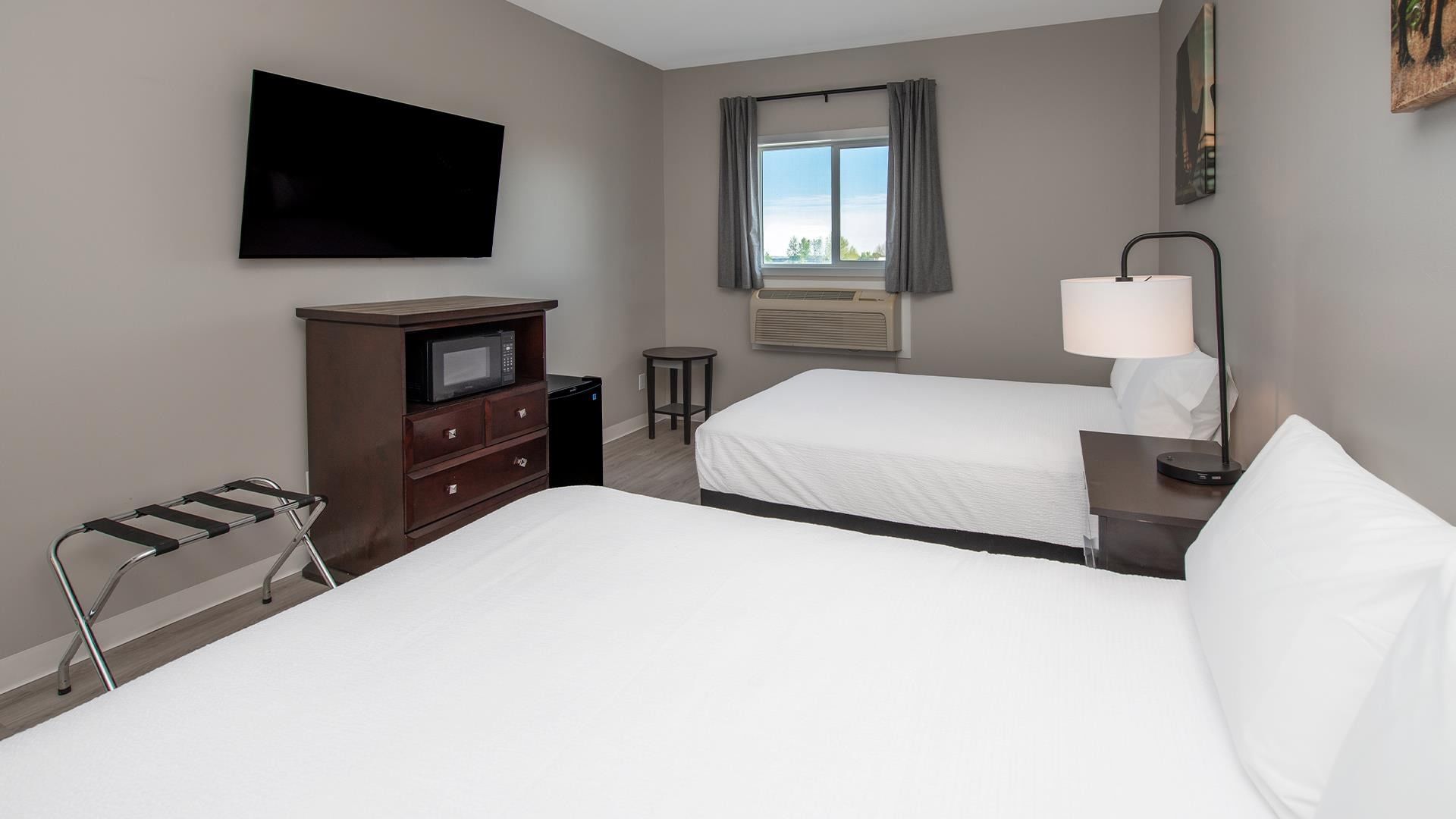Two beds with a TV, microwave, and window in a room at Coast Innisfail Hotel