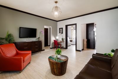 Modern living area at Tradewinds Apartment Hotel with an orange armchair, television, and views into the connected bedrooms