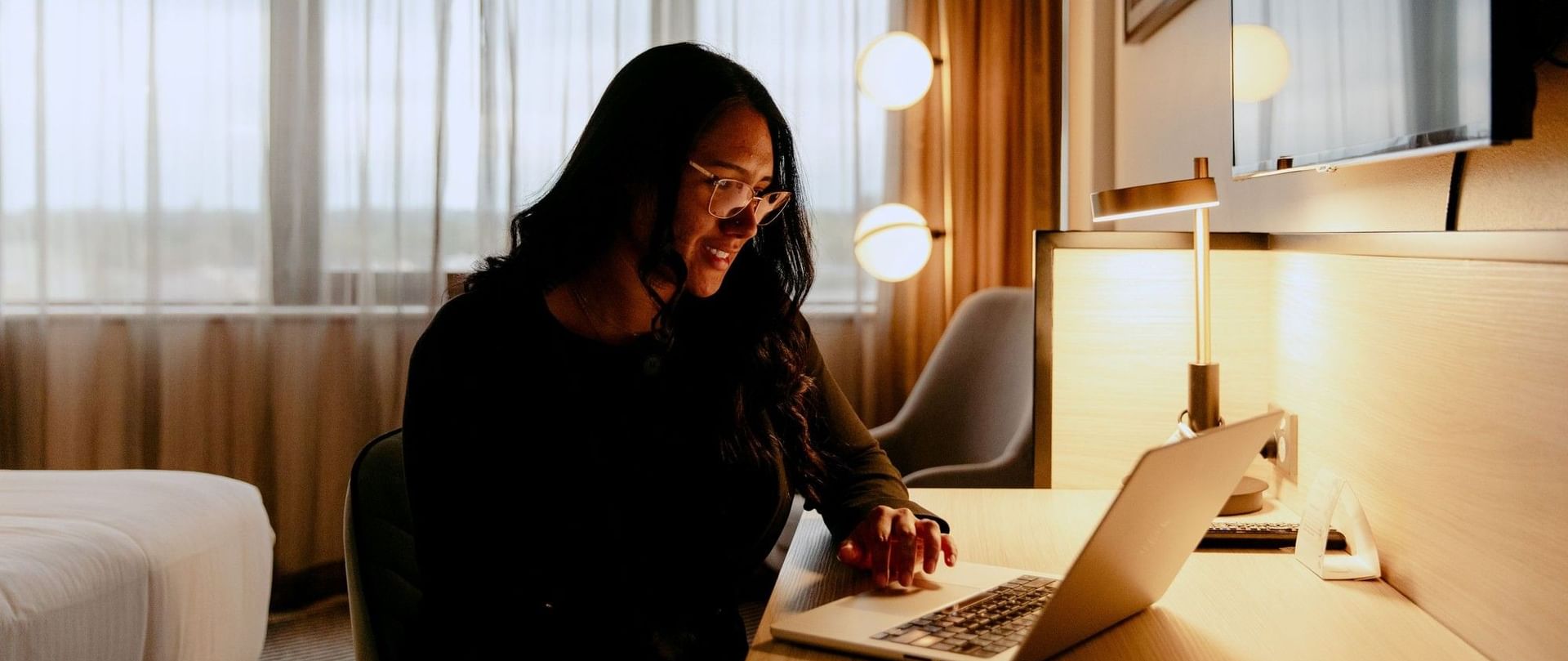 Woman smiling at laptop in a hotel room with a bed at Novotel Sydney Parramatta