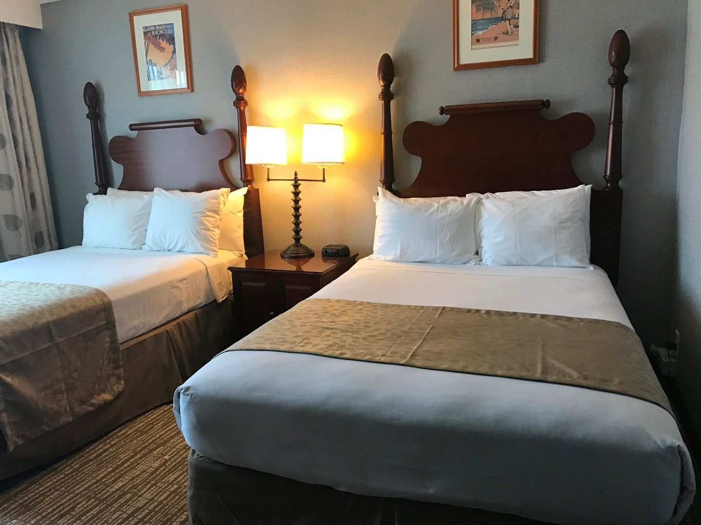 Two double beds with carved wooden headboards and white linens in Honolulu at Polynesian Residences