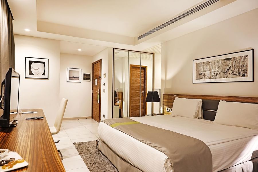 Bed by a wooden desk under minimalist art near a mirrored wardrobe in Deluxe Room at Warwick Stone 55 - Beirut
