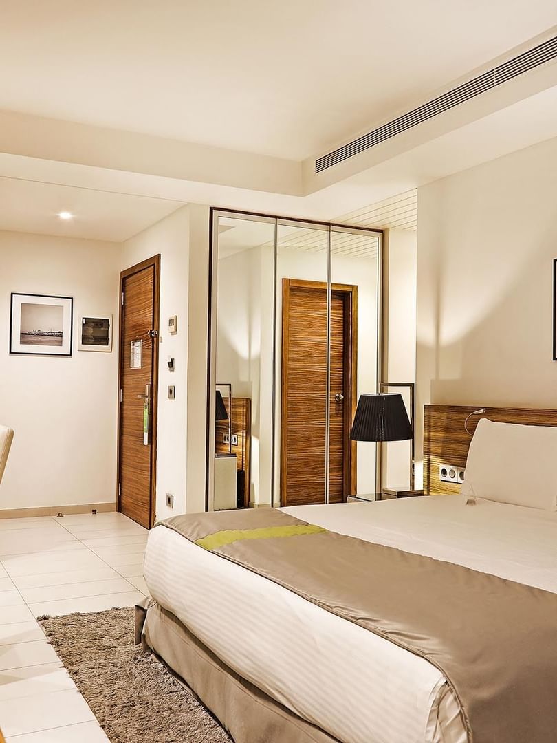 Bed by a wooden desk under minimalist art near a mirrored wardrobe in Deluxe Room at Warwick Stone 55 - Beirut