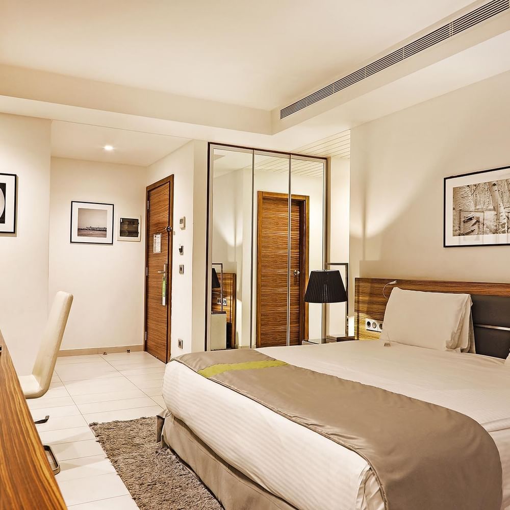 Bed by a wooden desk under minimalist art near a mirrored wardrobe in Deluxe Room at Warwick Stone 55 - Beirut
