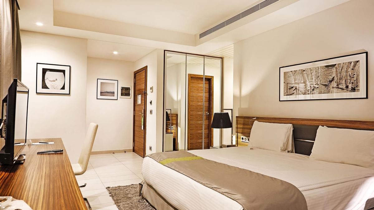 Bed by a wooden desk under minimalist art near a mirrored wardrobe in Deluxe Room at Warwick Stone 55 - Beirut