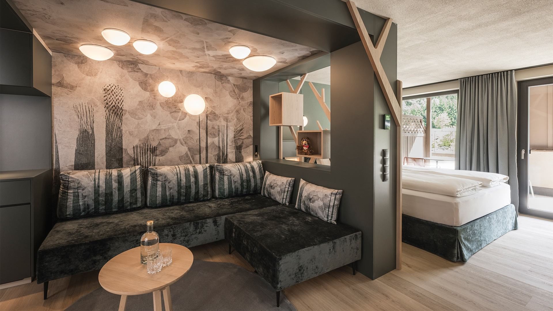 Modernes Zimmer mit Bett, Sofa, Tisch und Wandmalerei, beleuchtet durch Deckenleuchten.