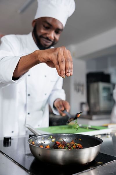 Chef seasoning a dish in the kitchen at Azalai Hotel Dakar