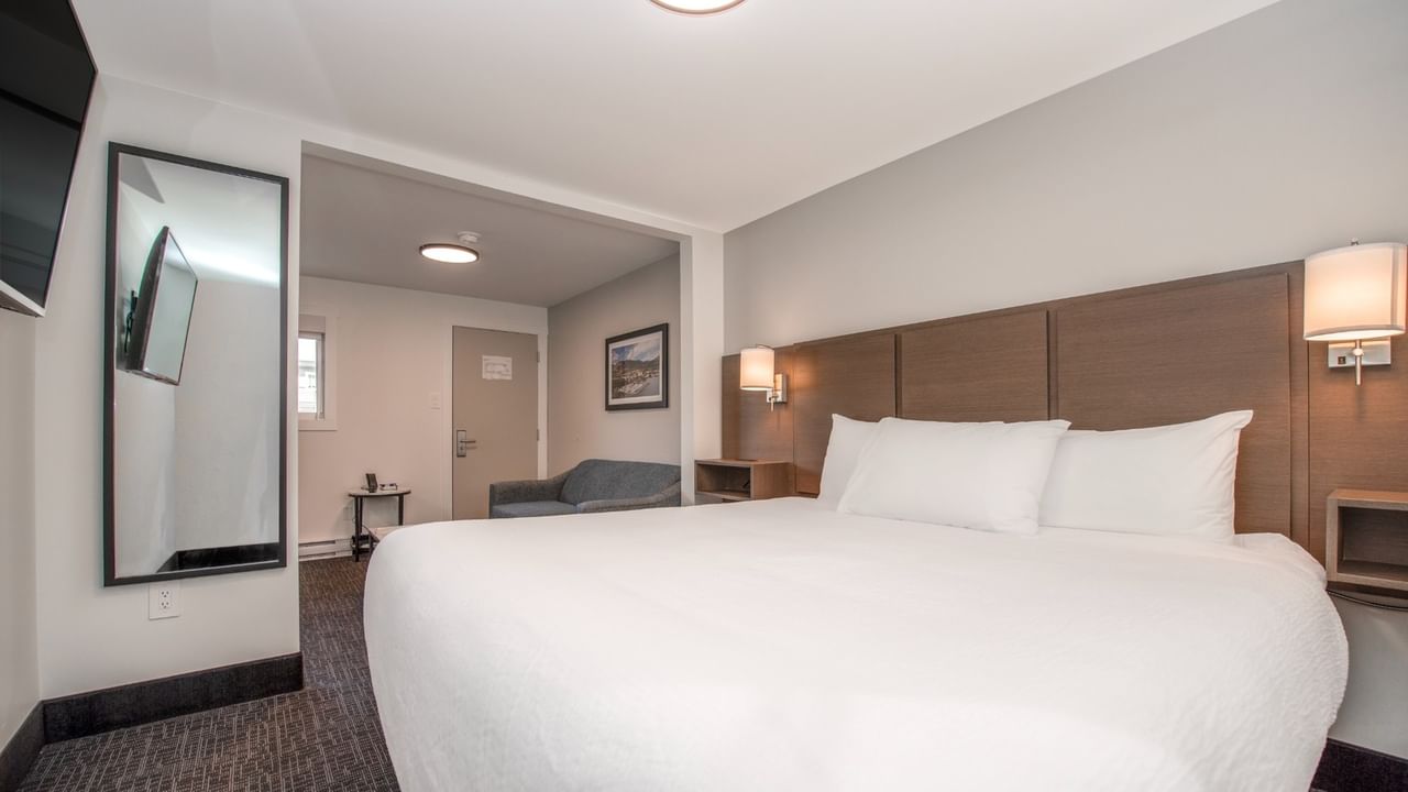 A hotel room with a large bed, two lamps, a couch, a mirror, and a TV.