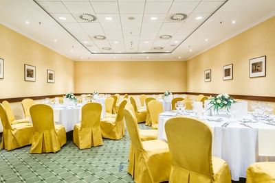 Dining room with yellow chair covers and tables adorned with glassware and floral centerpieces at Polonia Palace Hotel
