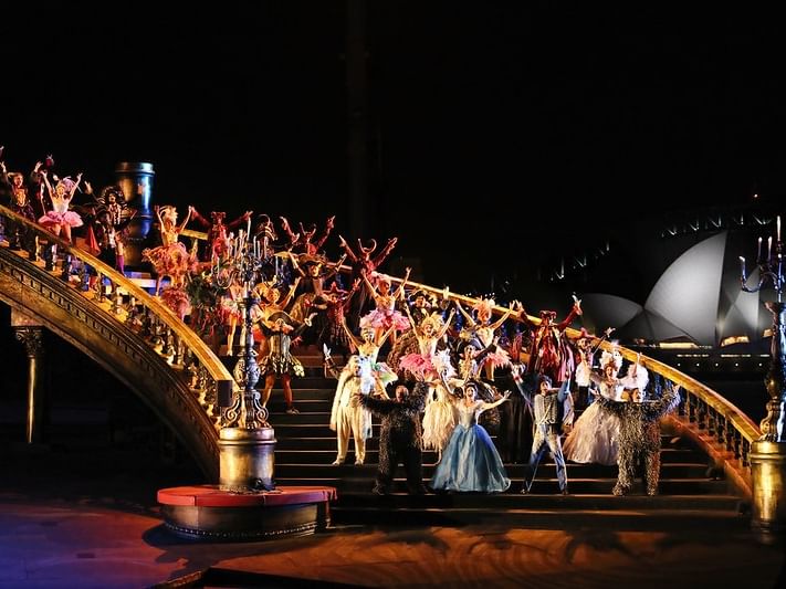 Performers in costumes on a grand staircase at night, with the Sydney Opera House in the background.