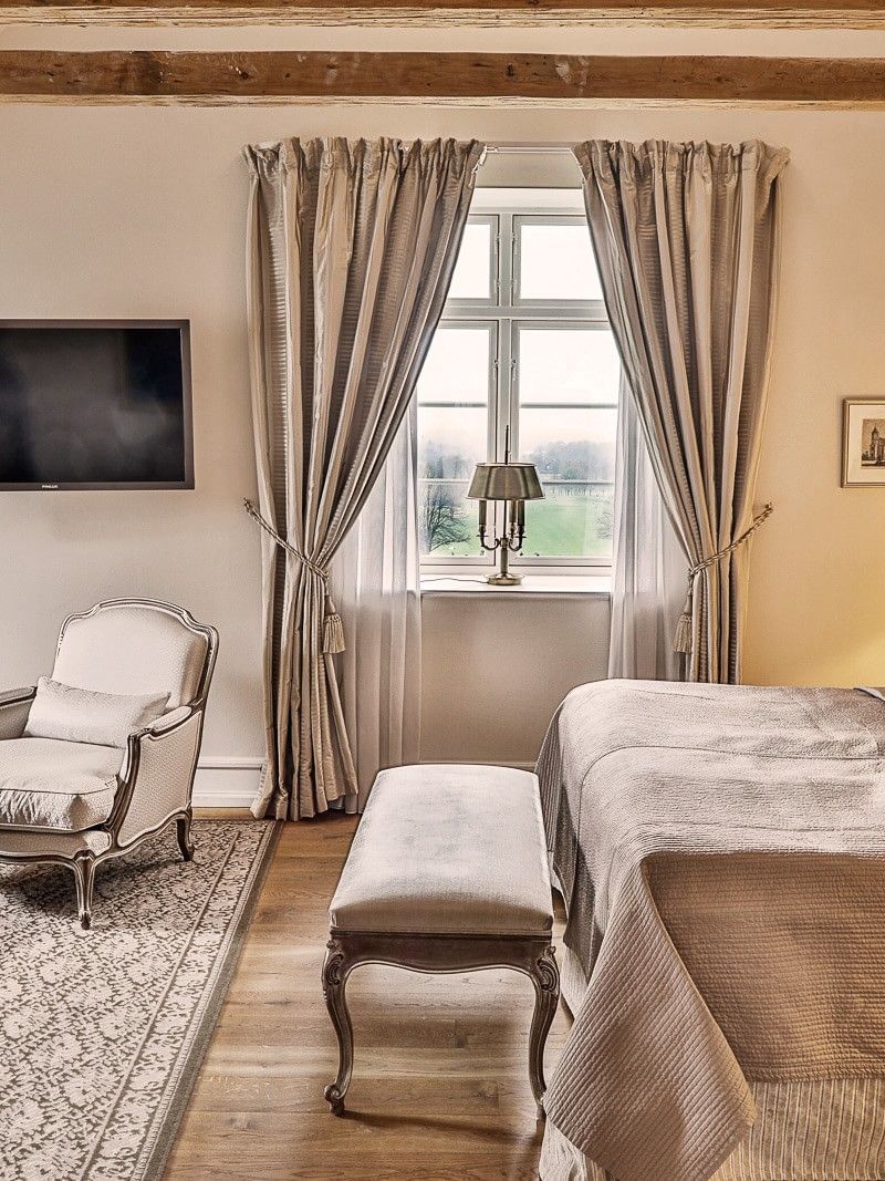 Junior suite featuring wooden ceiling beams and vintage desk, with plush bed at Warwick Denmark