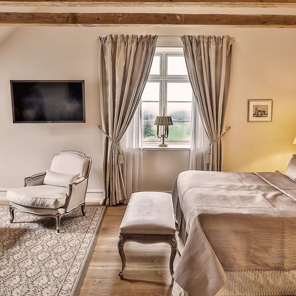 Junior suite featuring wooden ceiling beams and vintage desk, with plush bed at Warwick Denmark