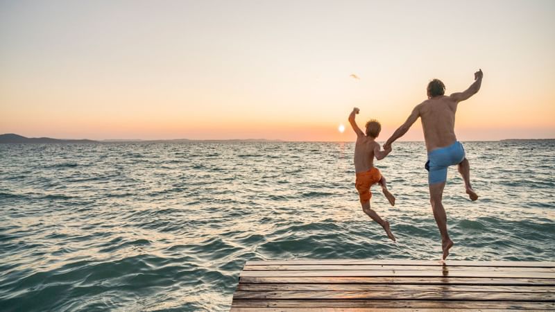 Father & son jumping to the sea near Falkensteiner Hotels