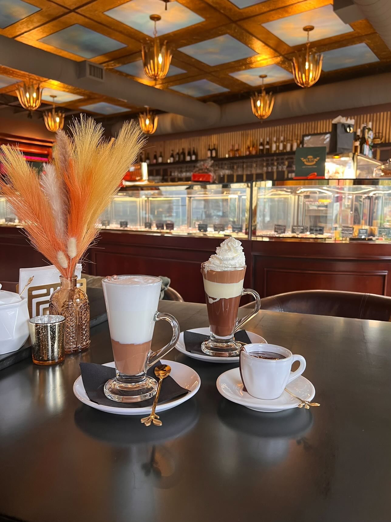 A cozy coffee shop table displaying two tall glass mugs of hot cocoa and one mug of thick hot chocolate, found at AJ Chocolate House.