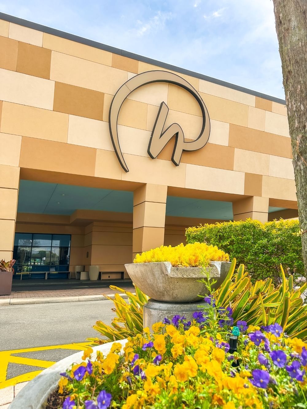 A low angle shot of the front entrance of Rosen Inn International, a family-friendly hotel in Orlando, with yellow and purple flowers in the front center of the frame.