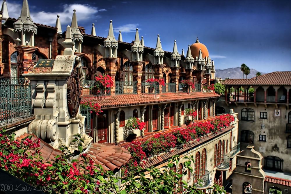 Red flowers by ornate balconies under spired rooftops surrounding the courtyard at Mission Inn Riverside, CA