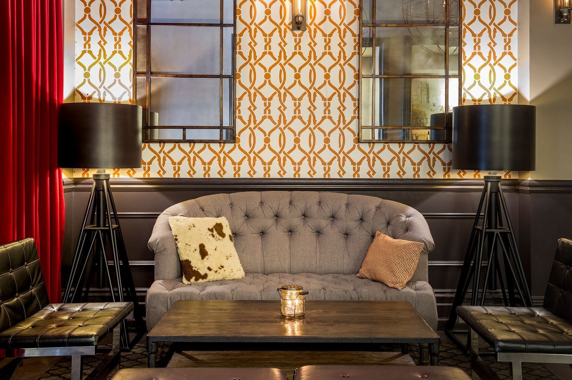 Grey sofa by tripod floor lamps under patterned wallpaper and mirrors in a lounge at Warwick San Francisco