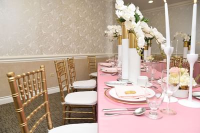 A pink table decorated with white flowers & gold wooden chairs in the Windsor Suite at Courtleigh Hotel & Suites