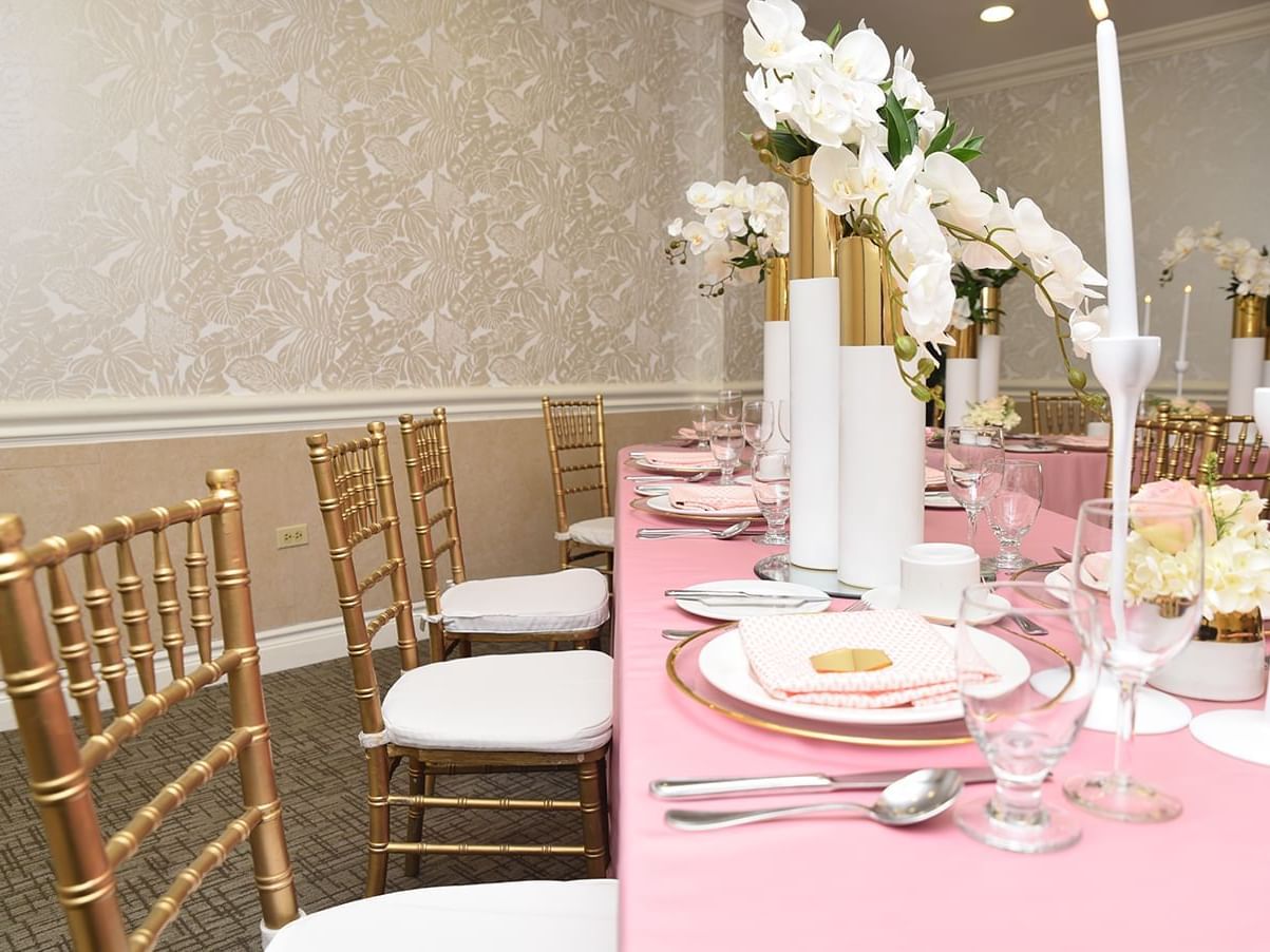 A pink table decorated with white flowers & gold wooden chairs in the Windsor Suite at Courtleigh Hotel & Suites