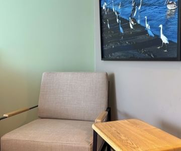 Upholstered armchair with wooden table beneath coastal seabird artwork on the accent wall at Unika Hotels