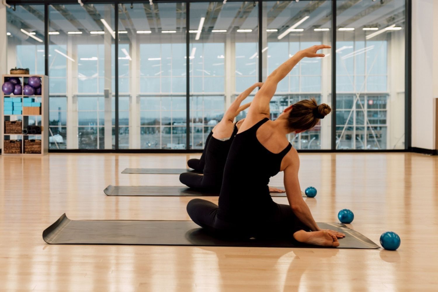 Women performing seated side stretches on exercise mats in a bright fitness studio with large windows at Hotel X Toronto