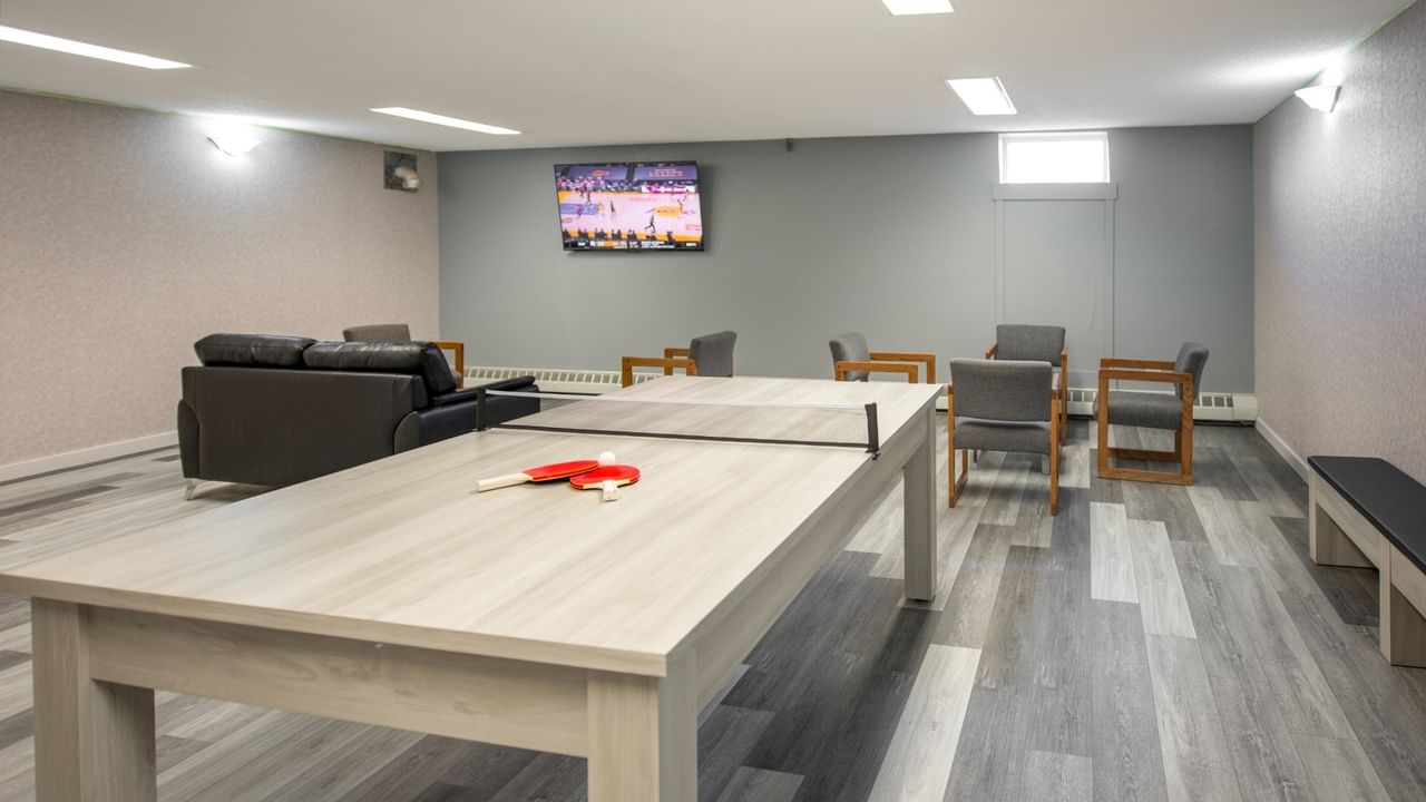 Recreation room with a ping pong table, chairs, couch, and TV showing a basketball game.