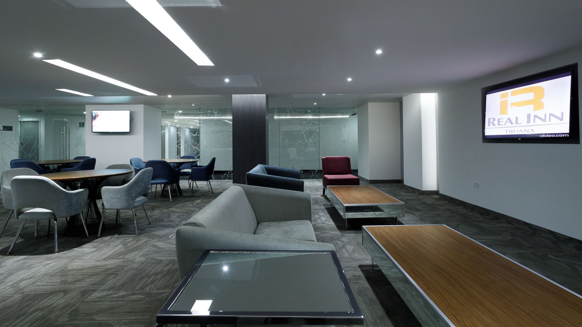 Quiet business lounge, with sleek furniture under soft lighting, and the brand logo on a screen at Real Inn Tijuana