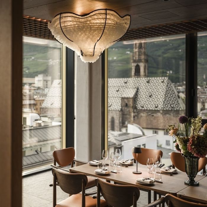 Elegantes Restaurant mit Panoramablick, Tisch und Stühlen, Kristallleuchter und Blumenarrangement.