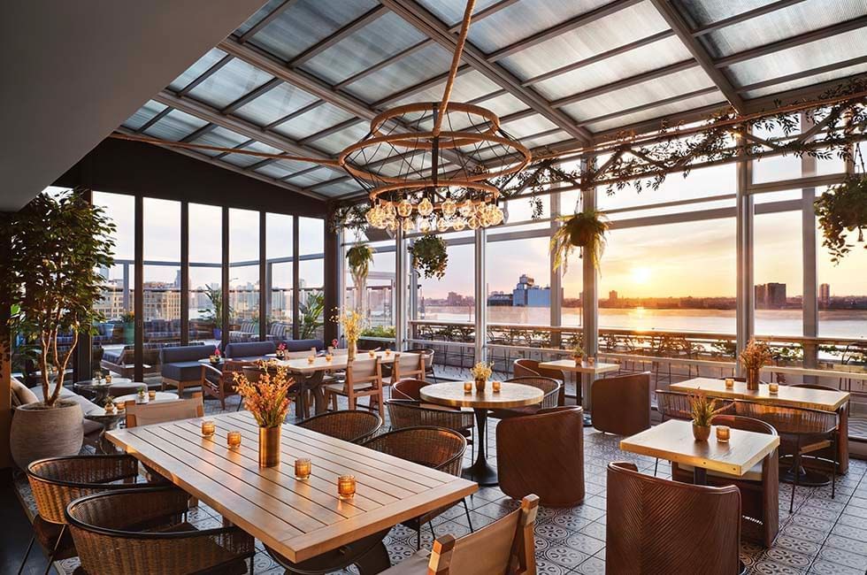 Gansevoort rooftop with tables and chairs overlooking the water during sunset.