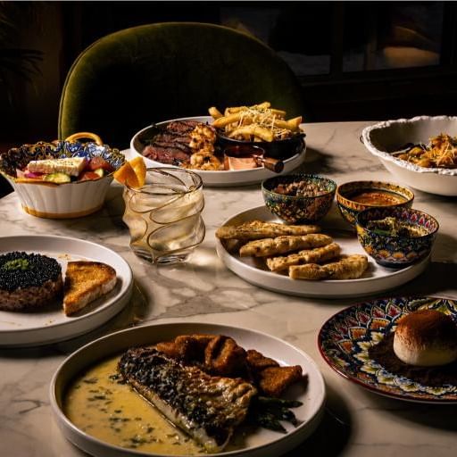 An elegant spread of gourmet dishes and cocktails arranged on a marble table for Raise a Glass to Miami Spice event