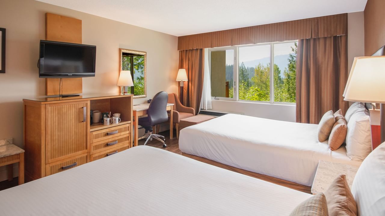 Hotel guest room with two queen beds, a work desk, TV, and arm chair