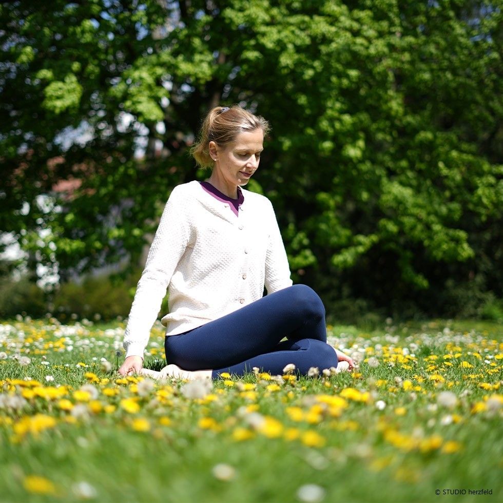Frau praktiziert Yoga auf einer blühenden Wiese unter Bäumen, Frühlingstagundnachtgleiche-Angebot.