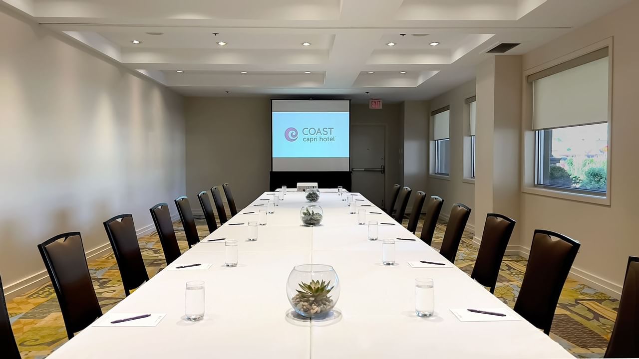 Long boardroom table set with water, pens and chairs facing presentation screen