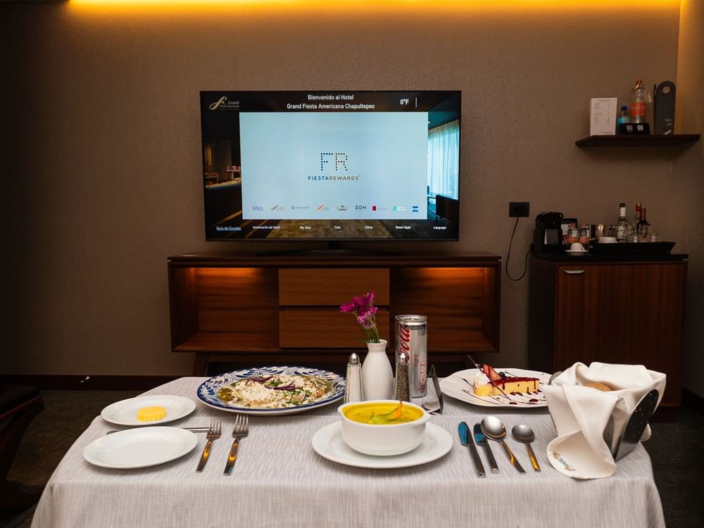 Table with food and drinks in front of a TV at Grand Fiesta Americana