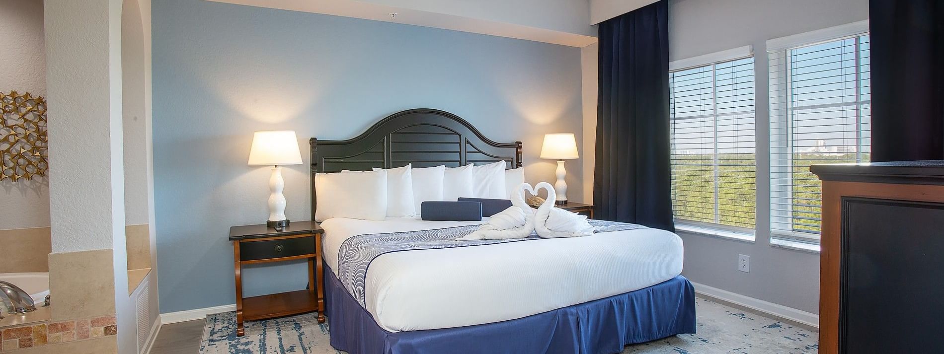 A hotel room with a large bed, two nightstands with lamps, and a window with blinds.