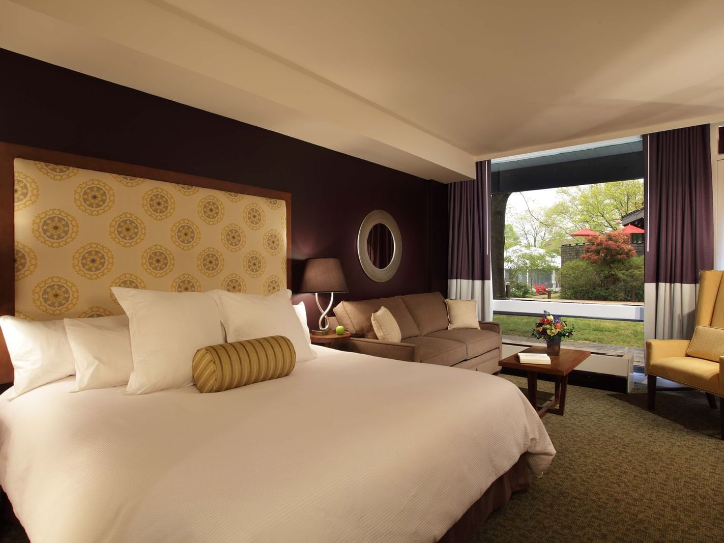 A luxurious King ADA hotel room at the Chauncey Conference Center with a king bed, couch, chair, and large window overlooking greenery.