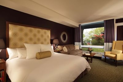 Guest room with patterned headboard, white bedding, seating area, and garden view at Aramark Chauncey Conference Center