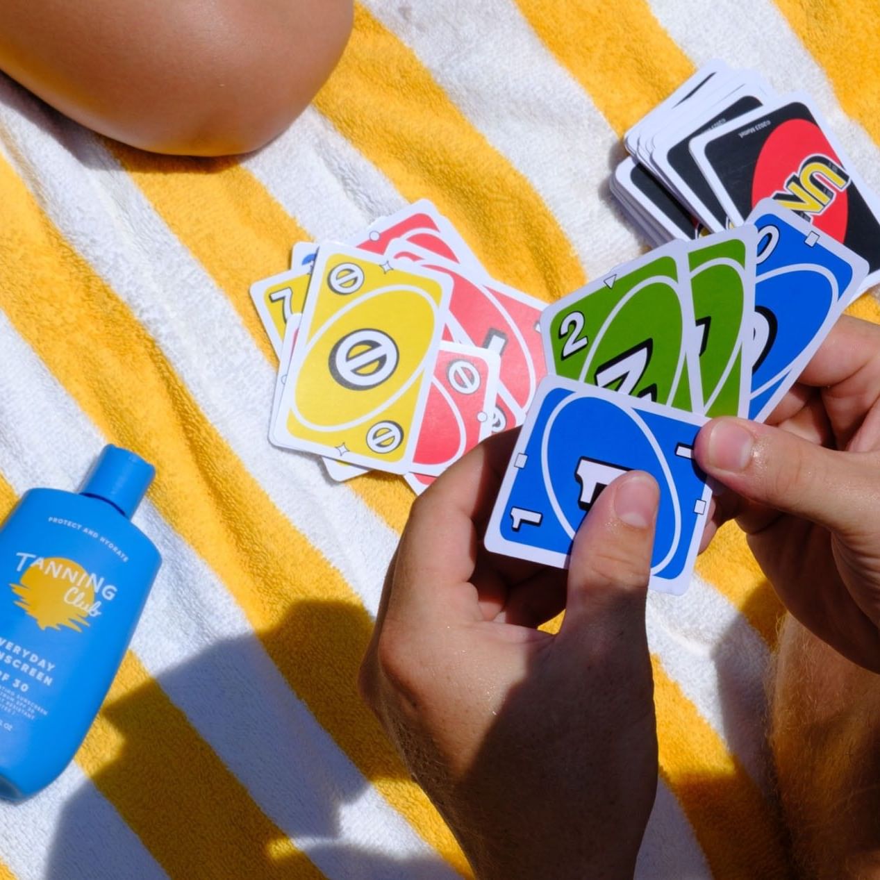 Playing a fun game of cards on a yellow and white striped towel while relaxing outdoors at Tradewinds Apartment Hotel