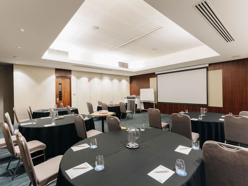 Round tables with chairs, glasses, and pitchers set up in Kaartdijinup I event rooms at Pullman Bunker Bay Resort, Naturaliste.