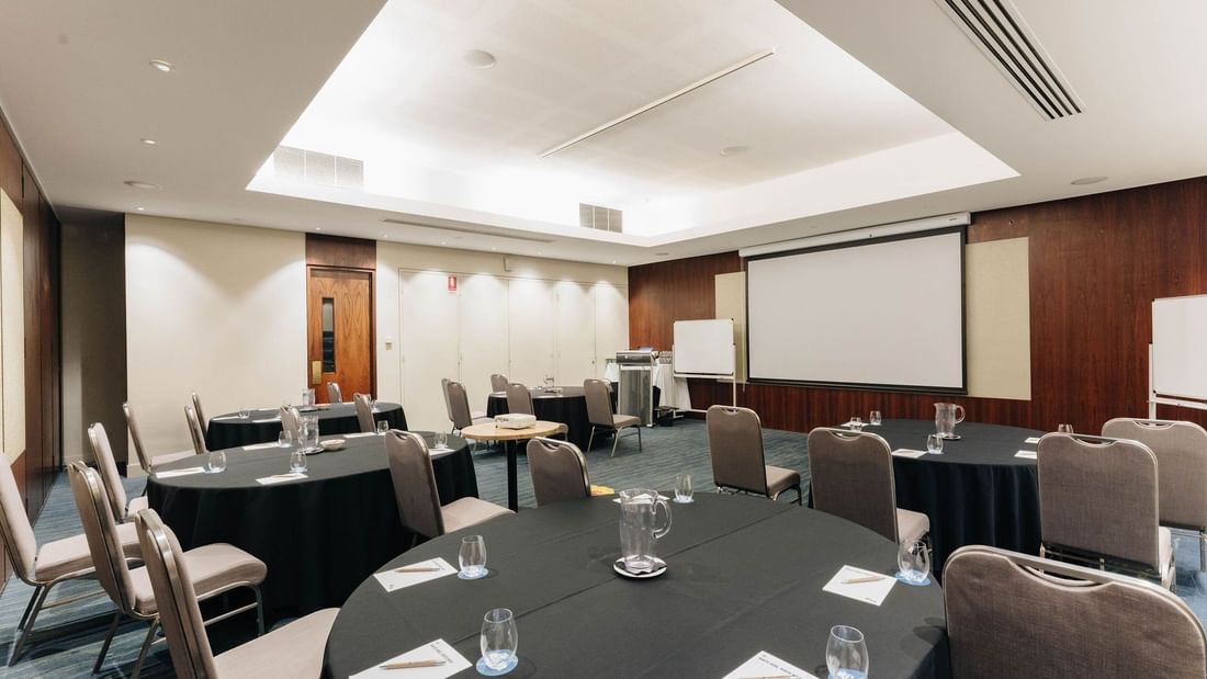 Round tables with chairs, glasses, and pitchers set up in Kaartdijinup I event rooms at Pullman Bunker Bay Resort, Naturaliste.